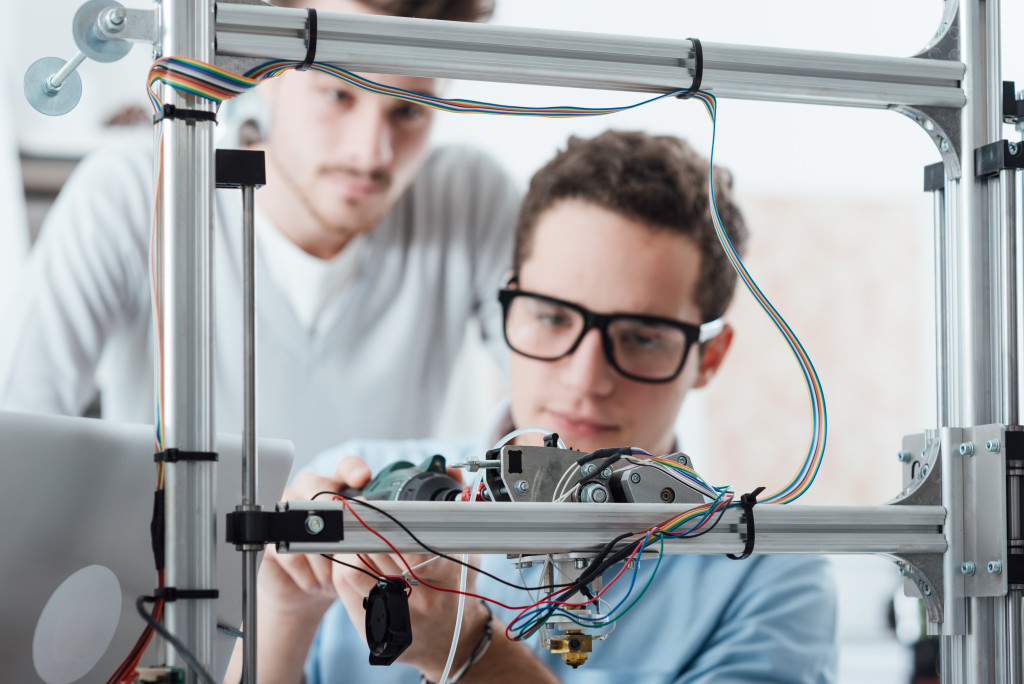 engineer in the lab adjusting a 3D printer's components, a student is watching